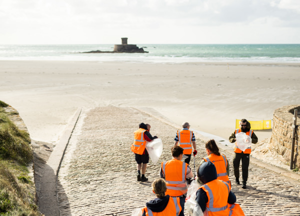 A group of people wearing high vis jackets, standing on a beach slip way with the sea behind them