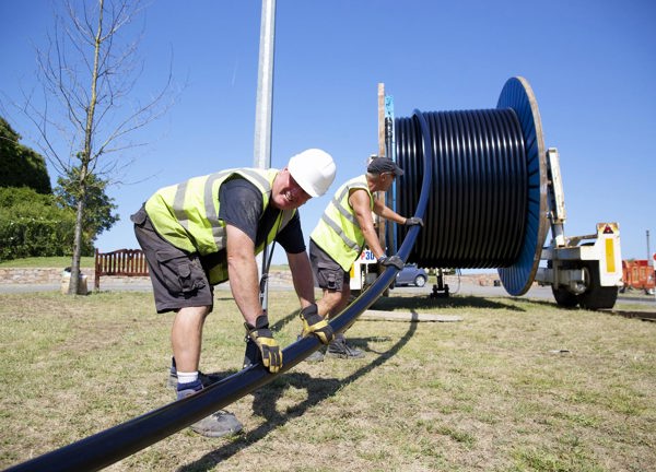 Two men guide power cable off a reel