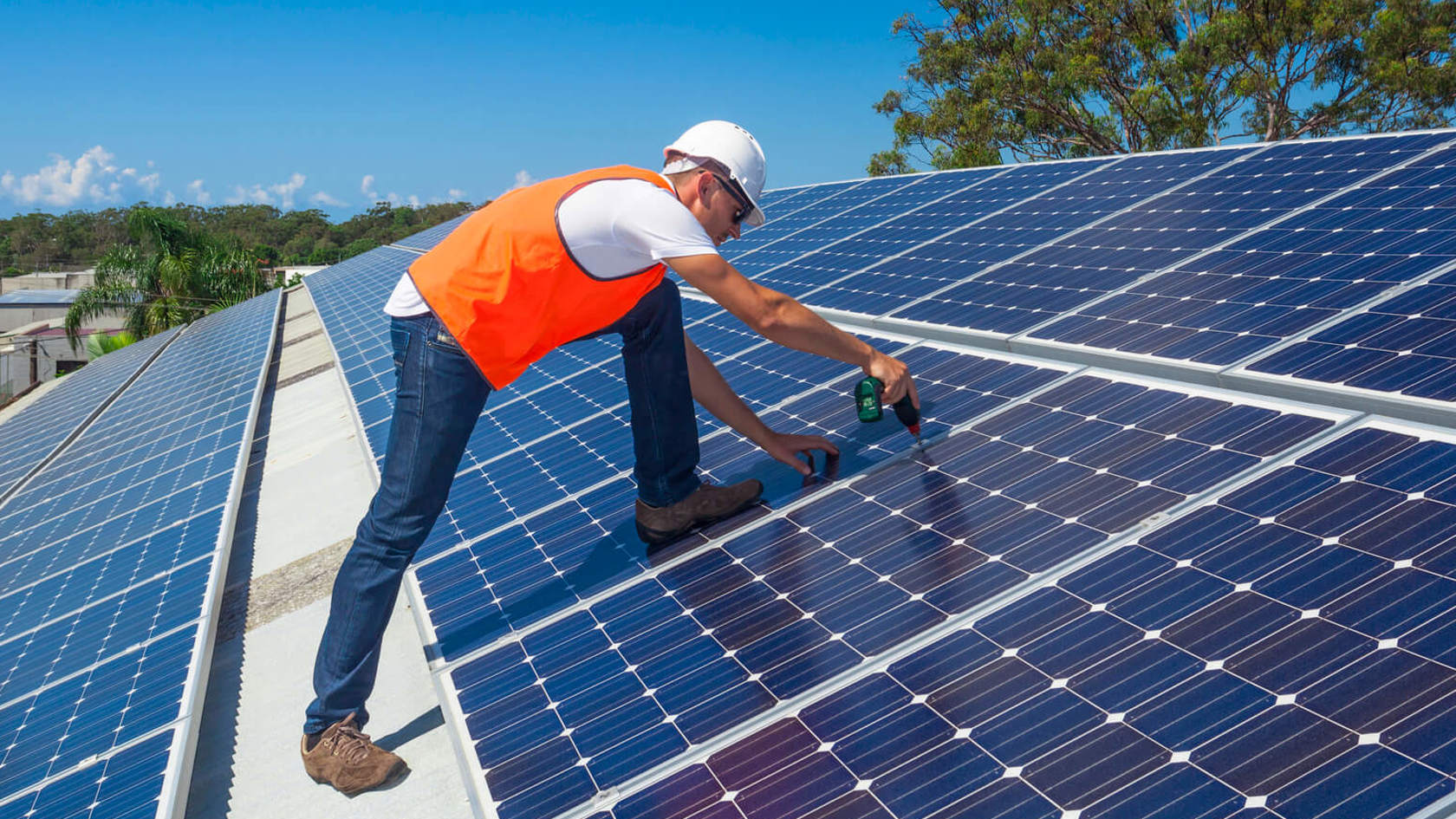A tradesperson installs solar panels on a large roof.