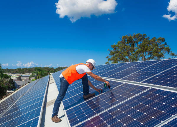 A tradesperson installs solar panels on a large roof.