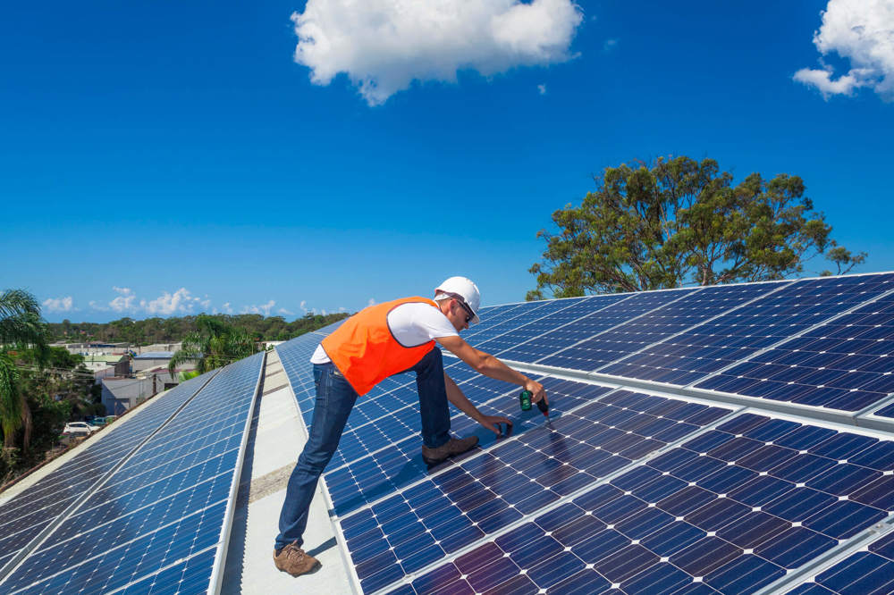 A tradesperson installs solar panels on a large roof.