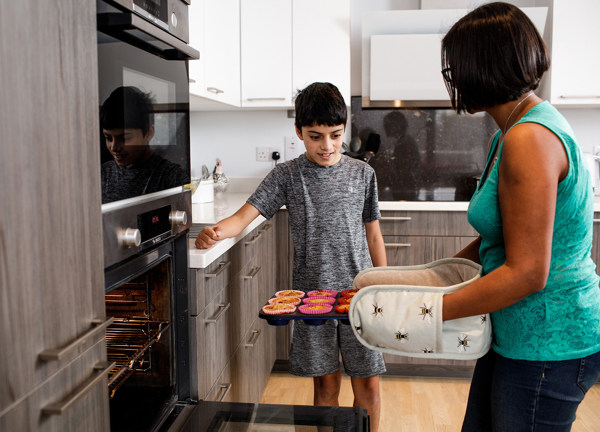 A mother removes her cupcakes from her electric oven as her son looks on.