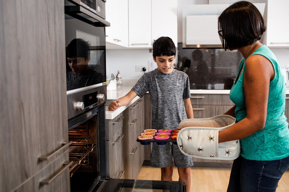 A mother removes her cupcakes from her electric oven as her son looks on.