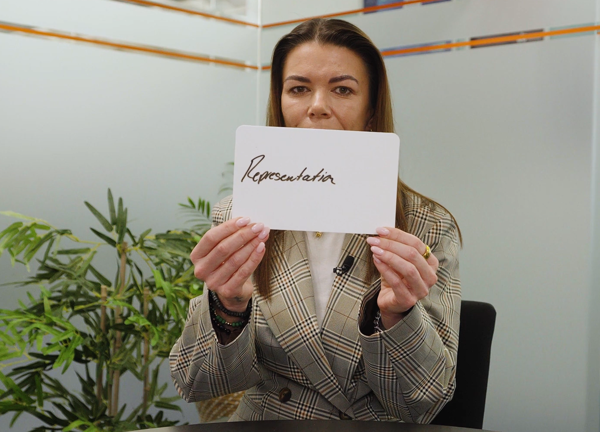 A person in an office setting holding a handwritten sign with the word 'representation'.