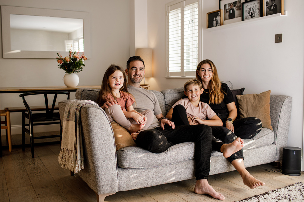 A family of four sit on the couch in their warm and cosy living room.