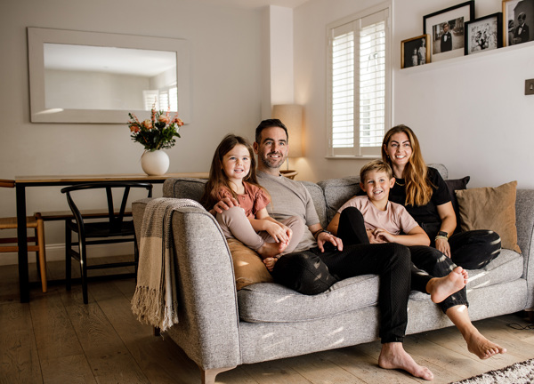 A family of four sit on the couch in their warm and cosy living room.