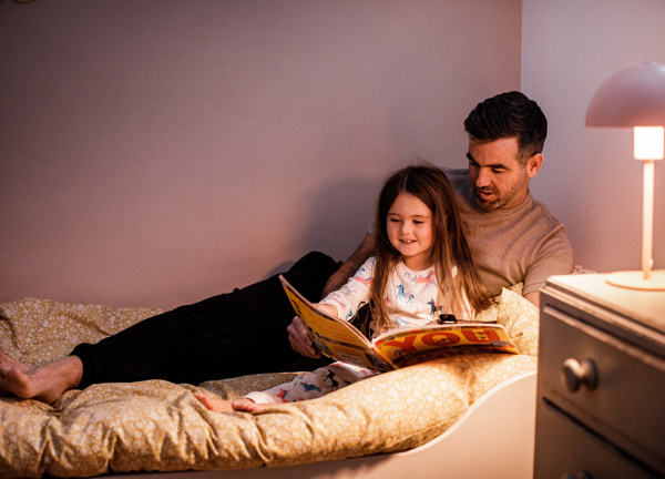 A father reads a story to his daughter in bed.