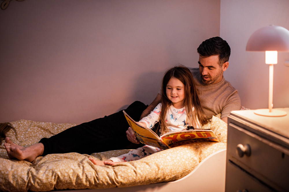 A father reads a story to his daughter in bed.